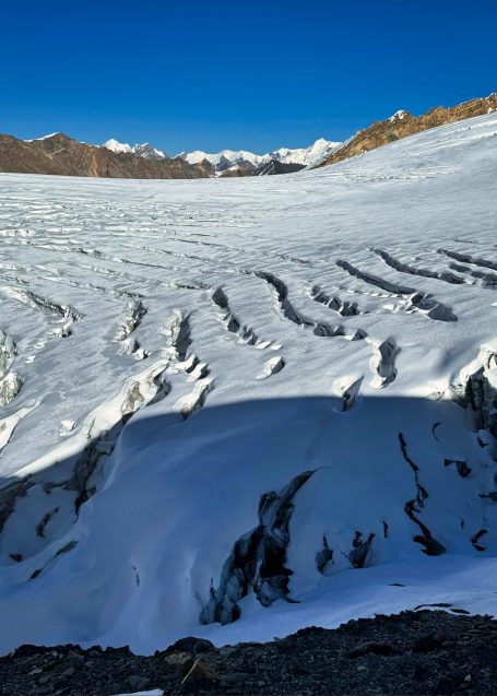 Schneebedeckter Gletscher mit zerklüfteter Oberfläche und Bergen im Hintergrund.