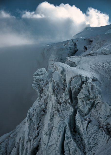 Schneebedeckte Klippen mit Wolken und Nebel im Hintergrund.