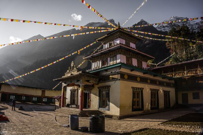 Buddhistischer Tempel mit bunten Fähnchen vor bergiger Kulisse.