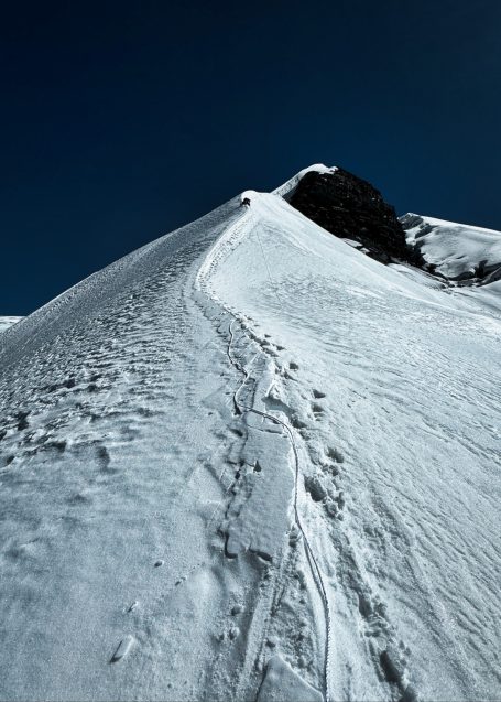 Schneebedeckter Berggipfel mit Fußspuren im Schnee und klarem, blauem Himmel.