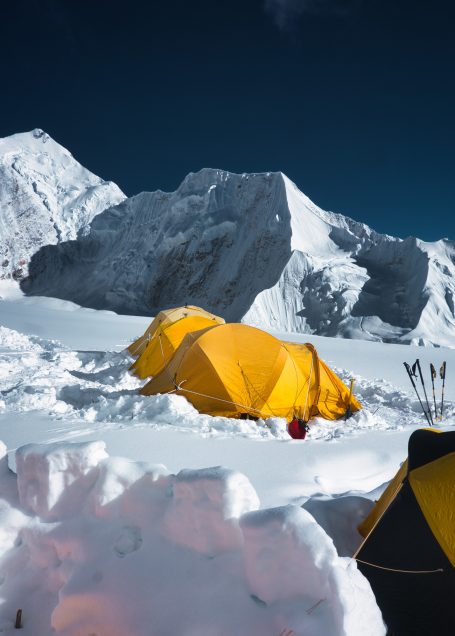 Zwei gelbe Zelte liegen in einer schneebedeckten Gebirgslandschaft.