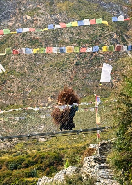 Ein Mensch in traditioneller Tracht geht über eine Hängebrücke in den Bergen.