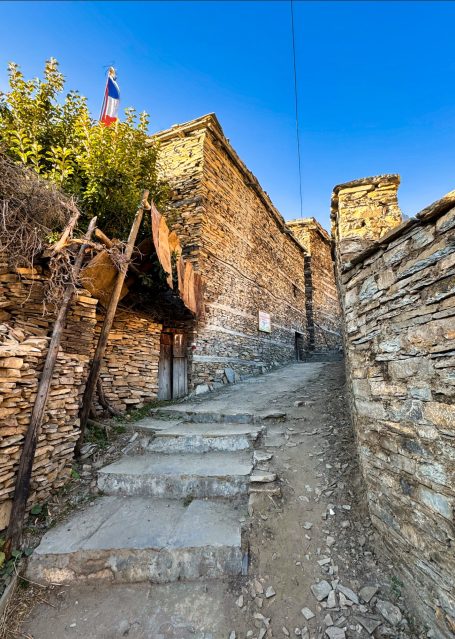 Steinerner Weg mit Stufen, umgeben von alten Mauern und Bäumen, blauem Himmel im Hintergrund.