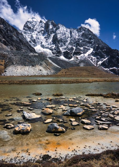 Berglandschaft mit schneebedeckten Gipfeln und steiniger Uferlandschaft.