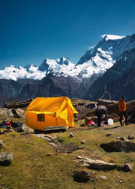Ein gelbes Zelt in den Bergen mit schneebedeckten Gipfeln im Hintergrund.
