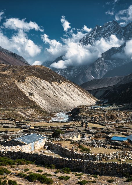 Berglandschaft mit Fluss, Wolken und kleinen Siedlungen im Tal.
