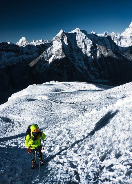 Ein Bergsteiger in leuchtend gelber Kleidung wandert auf schneebedecktem Terrain.