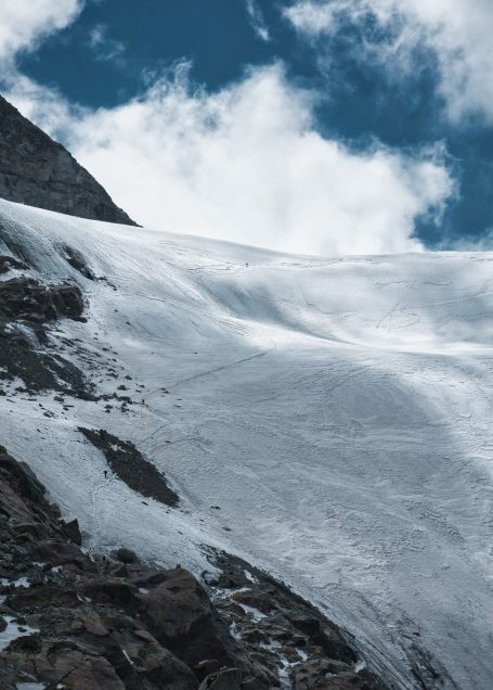Eisige Berglandschaft mit Schneefeld und vereinzelten Wolken am blauen Himmel.