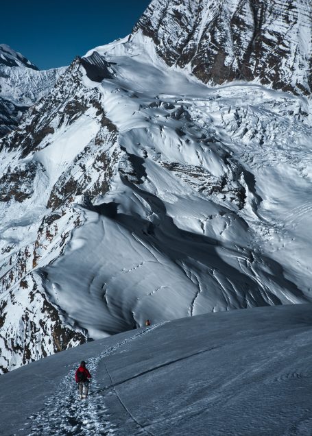 Schneebedeckter Berg mit einem Wanderer im Vordergrund und majestätischen Gipfeln im Hintergrund.