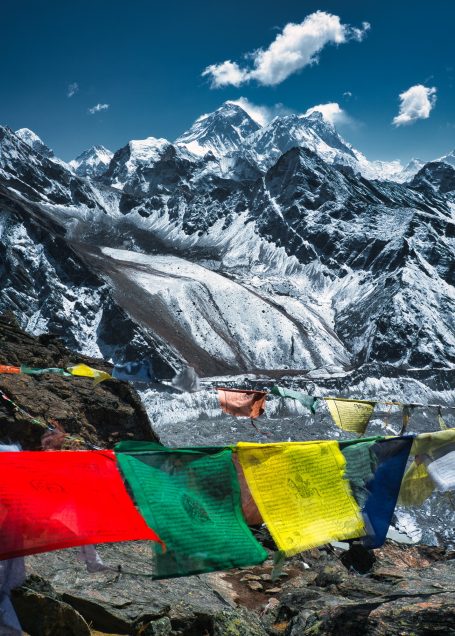 Bunte Gebetsfahnen vor schneebedeckten Bergen und einem Gletscher unter klarem Himmel.