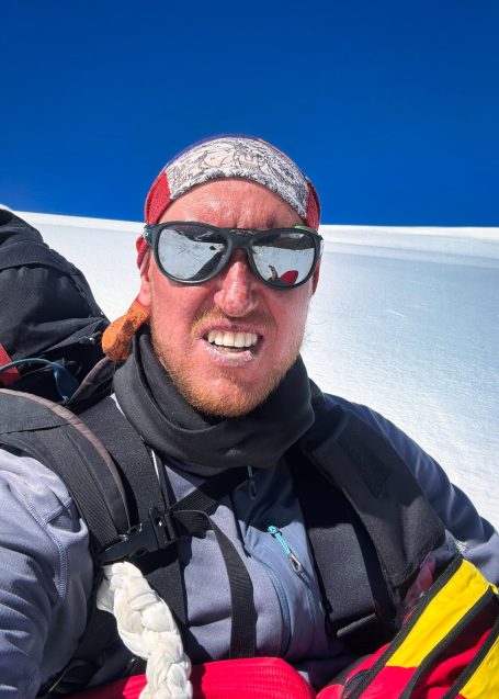 Mann mit Sonnenbrille und Kopfband, in Bergwanderausrüstung auf Schnee.