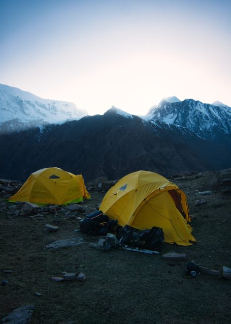 Zwei gelbe Zelte in einer bergigen Landschaft bei Sonnenaufgang.