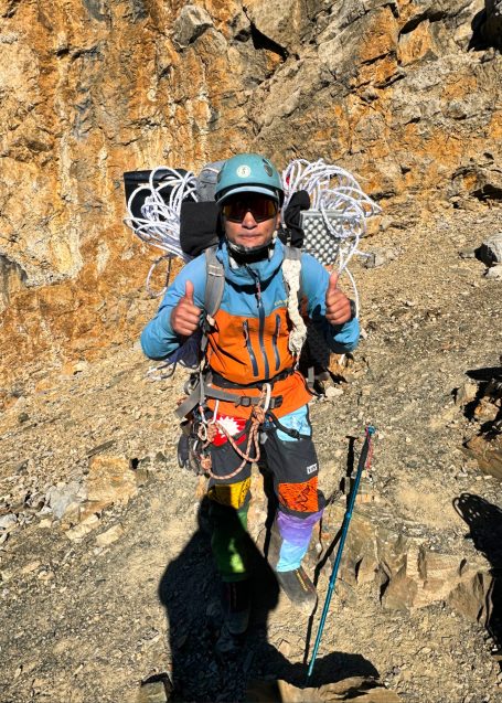 Bergsteiger in bunter Ausrüstung steht auf felsigem Terrain.