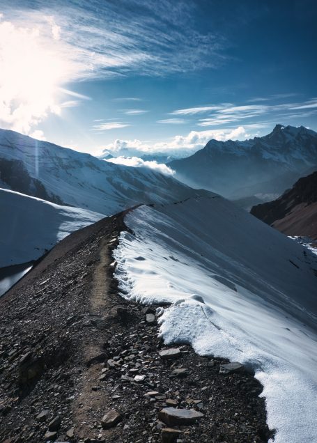 Ein schmaler Pfad führt über schneebedeckte Berge unter klarem Himmel.