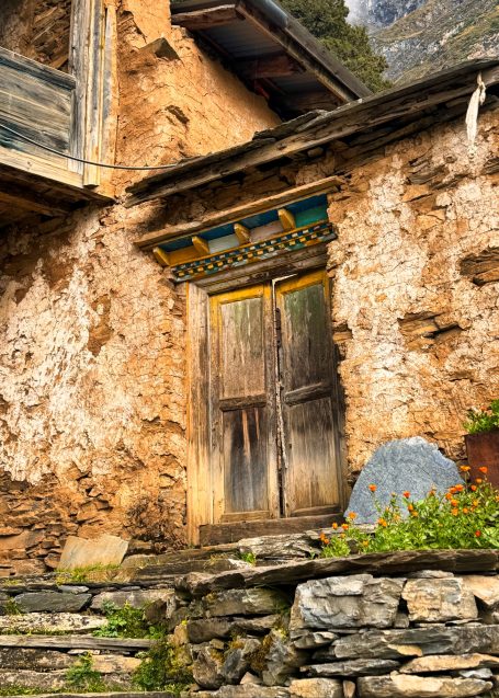 Tür in einer alten, verfallenen Wand aus Stein und Erde, umgeben von Blumen.