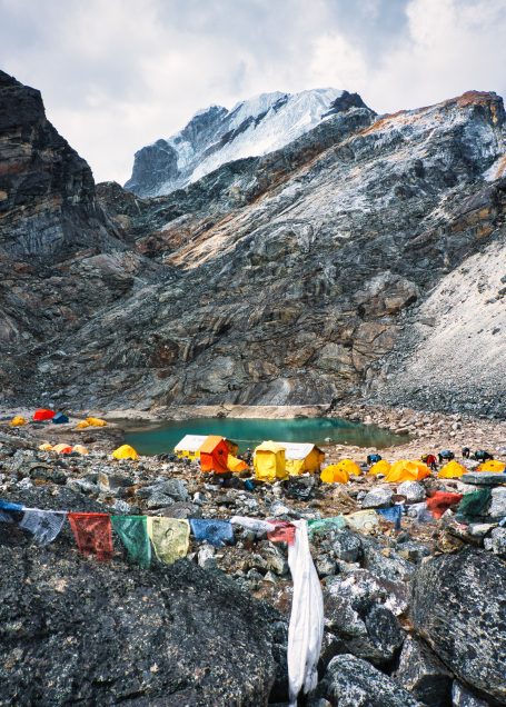 Bunte Zelte am Ufer eines klaren Gebirgssees, umgeben von felsigen Berghängen.