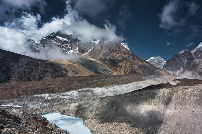 Berglandschaft mit schneebedeckten Gipfeln, Wolken und einem Gletscher.