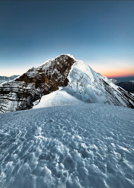 Schneebedeckter Berggipfel bei Sonnenaufgang mit klarem Himmel im Hintergrund.