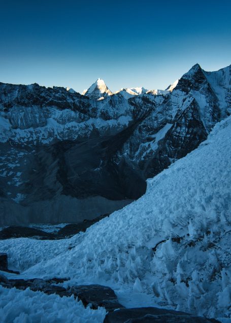 Berglandschaft bei Dämmerung, schneebedeckte Gipfel im Hintergrund, klare blaue Himmel.
