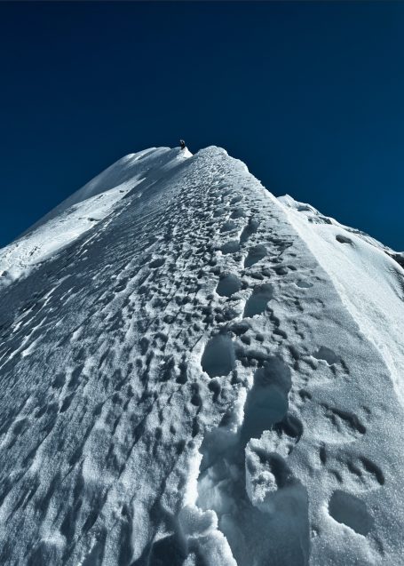 Eine mit Fußspuren bedeckte, steile Schneepiste unter einem klaren, blauen Himmel.