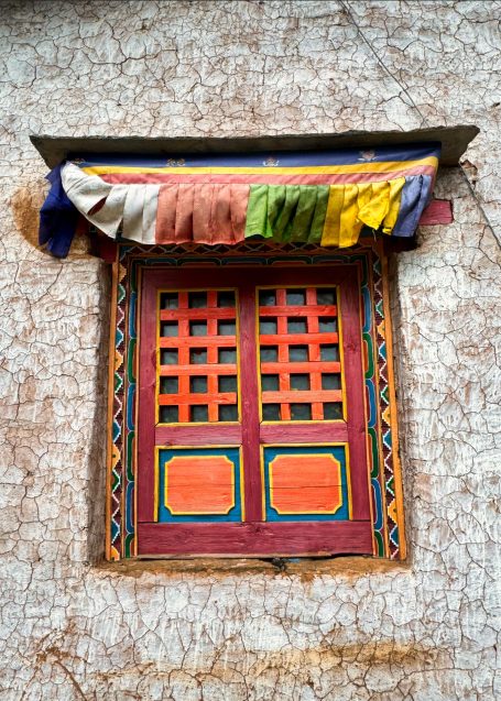 Bunte Fenster mit quadratischen Gittern und bunten Stoffen darüber an einer Wand.