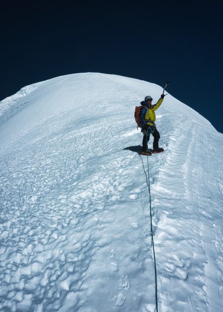 Ein Bergsteiger klettert auf einer schneebedeckten Gipfelkuppe.