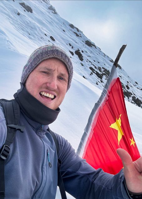 Person im Schnee mit einem roten Flaggenhintergrund und lächelndem Gesicht.