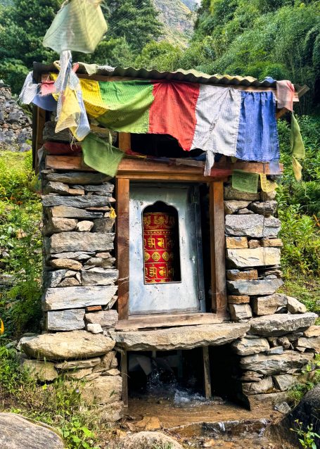 Steinerne Hütte mit bunten Gebetsfahnen und einem geschlossenen Holzportal.