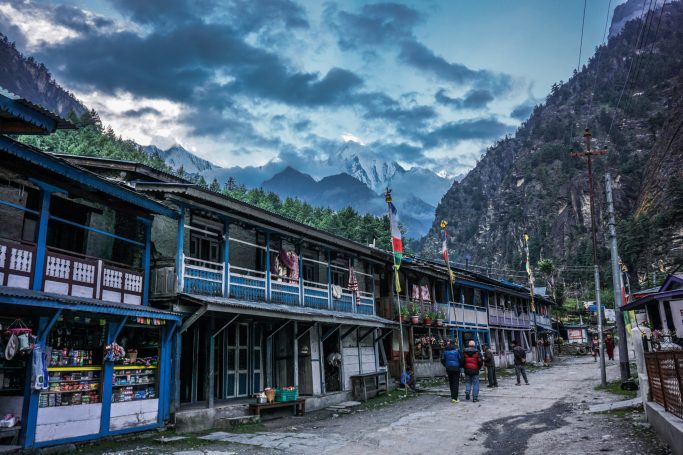 Bergdorf mit traditioneller Architektur und dramatischem Himmel, umgeben von hohen Bergen.