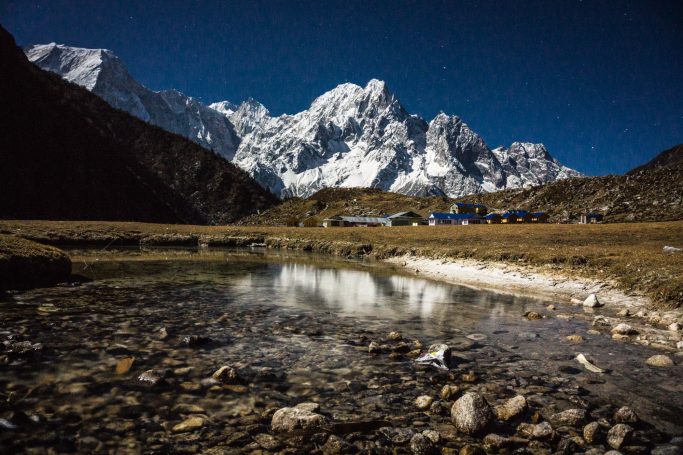 Berglandschaft mit schneebedeckten Gipfeln und glasklarem Wasser im Vordergrund.