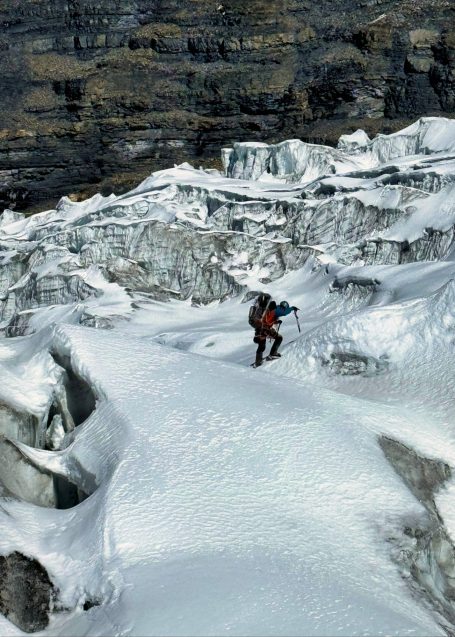 Ein Bergsteiger wandert über einen gefrorenen Gletscher in einer felsigen Gebirgslandschaft.