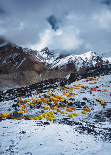 Bunte Zelte in einer schneebedeckten Berglandschaft unter bewölktem Himmel.