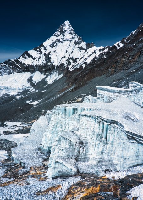 Hoher Berg mit schneebedecktem Gipfel und eisigen Gletschern im Vordergrund.