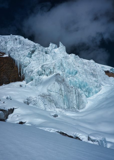 Große Eismasse mit schneebedecktem Boden und dramatischem Himmel im Hintergrund.