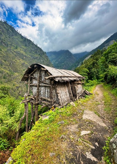 Alter, verfallener Holzbau auf einem Hügel, umgeben von Bergen und üppiger Vegetation.
