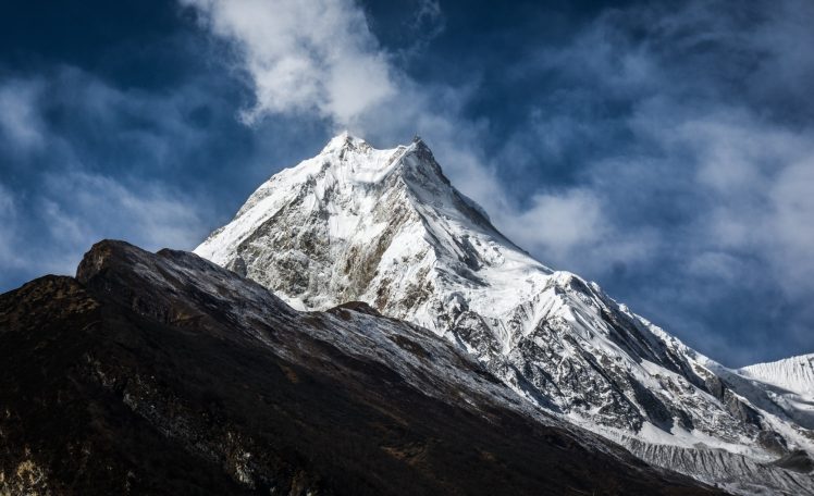Hoher, schneebedeckter Berggipfel unter einem bewölkten Himmel.
