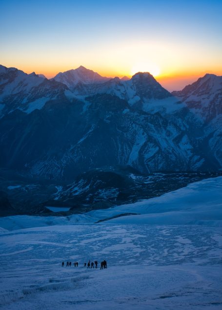 Sonnenaufgang über schneebedeckten Bergen mit sanften Hügeln im Vordergrund.