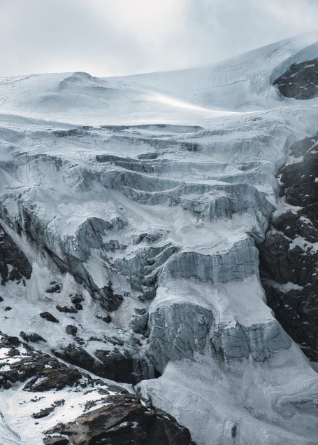 Gletscher mit eisbedeckten Felsen und eisigen Schichten, umgeben von Bergen.