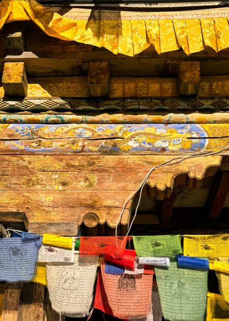 Bunt gefaltete Gebetsfahnen und bemaltes Holz an einem traditionellen Gebäude.