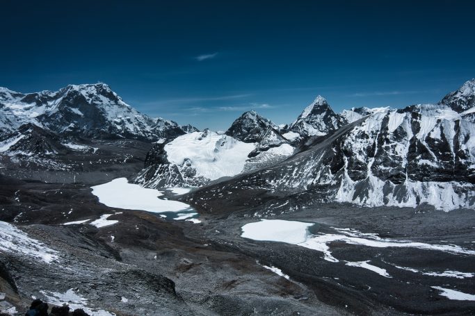 Berglandschaft mit schneebedeckten Gipfeln und Gletschern unter blauem Himmel.