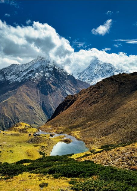 Berglandschaft mit schneebedeckten Gipfeln, grünen Hängen und einem klaren See.
