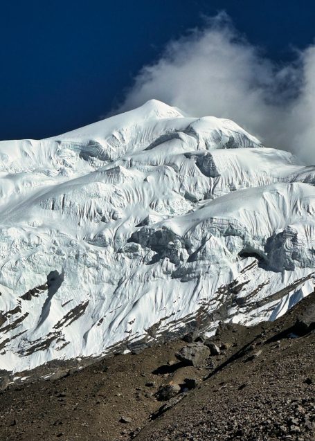Schneebedeckte Bergspitze mit Wolken und felsiger Unterlage.