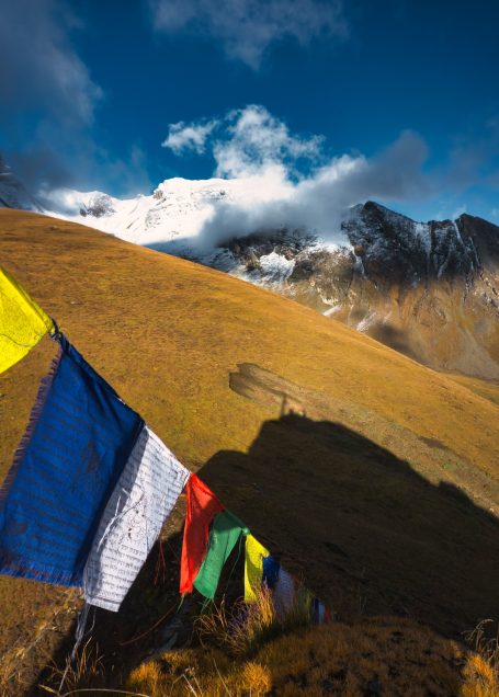 Bunte Gebetsfahnen wehen vor einer Berglandschaft unter blauem Himmel.