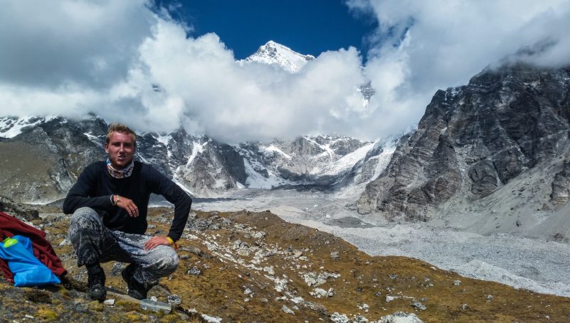 Ein Mann posiert in den Bergen mit schneebedeckten Gipfeln im Hintergrund.