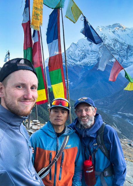 Drei Männer posieren vor schneebedeckten Bergen und Fahnen in den Himalaya.