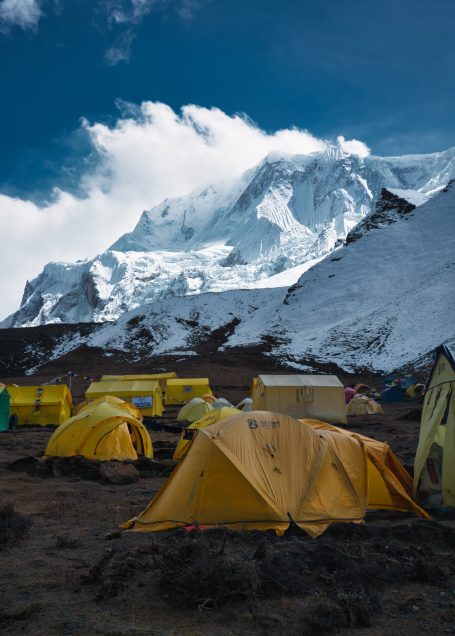 Bunte Zelte vor schneebedecktem Berg unter einem blauen Himmel mit Wolken.