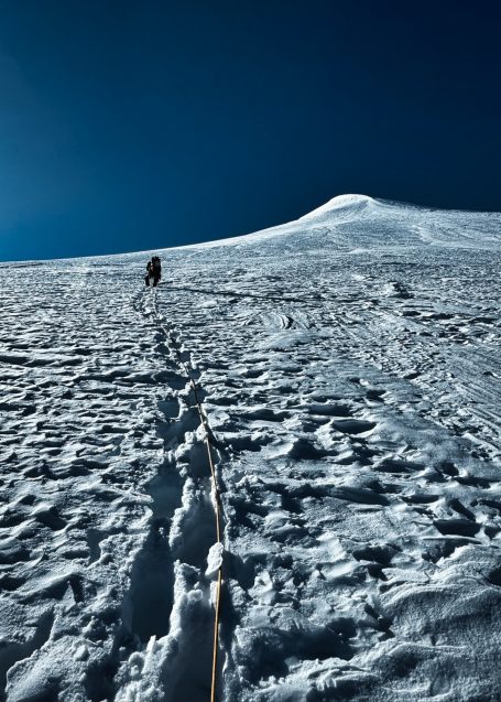 Bergsteiger erklimmt schneebedeckten Hang unter klarem, blauem Himmel.