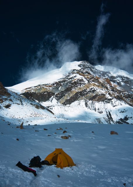 Ein Zelt auf Schneefeld vor einem schneebedeckten Gebirgszug unter klarem Himmel.