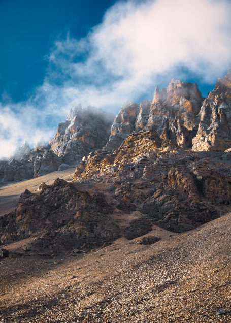 Hohe, felsige Berge mit Wolken und blauem Himmel im Hintergrund.