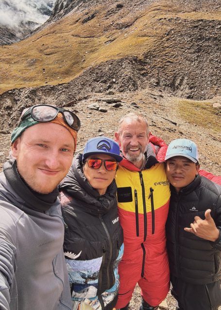 Vier Personen posieren in Berglandschaft, alle tragen Outdoor-Bekleidung und lächeln.